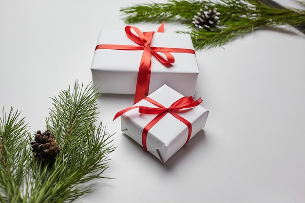 Scatole regalo di Natale con nastro rosso e ramo di pino verde con coni sul tavolo bianco