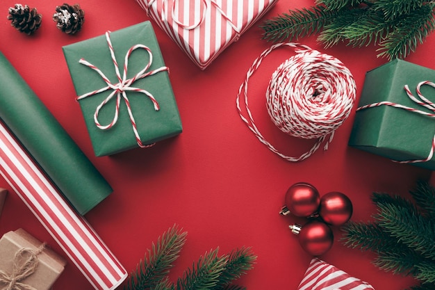 Scatole regalo di Natale con rotoli di carta e decorazioni su sfondo rosso piatto