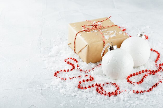 Scatole regalo di Natale in carta kraft, perline rosse, palline di Natale bianche e rami di abete su un tavolo innevato