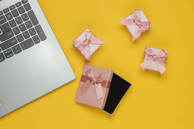 Scatole regalo e laptop con fiocco su sfondo giallo. Composizione per natale, compleanno o matrimonio. Vista dall'alto