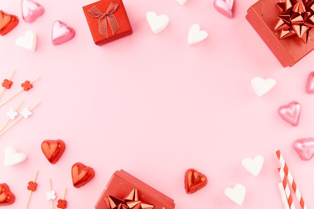 Scatole regalo rosse con nastri caramelle a forma di cuore marshmallows e decorazioni di carta cuore su rosa