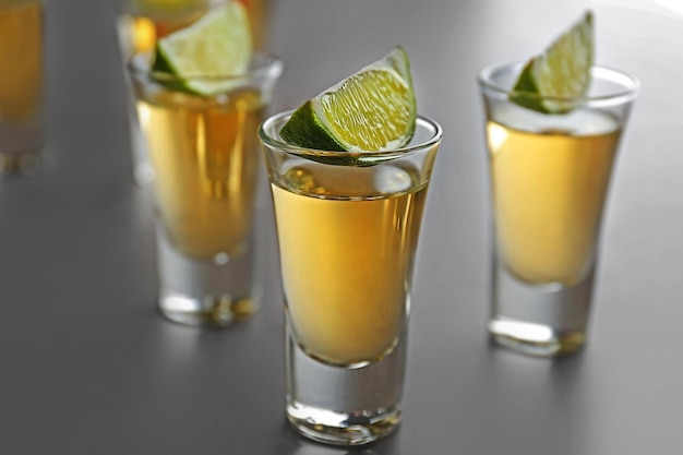 Scatti di tequila dorata con fette di lime su sfondo chiaro