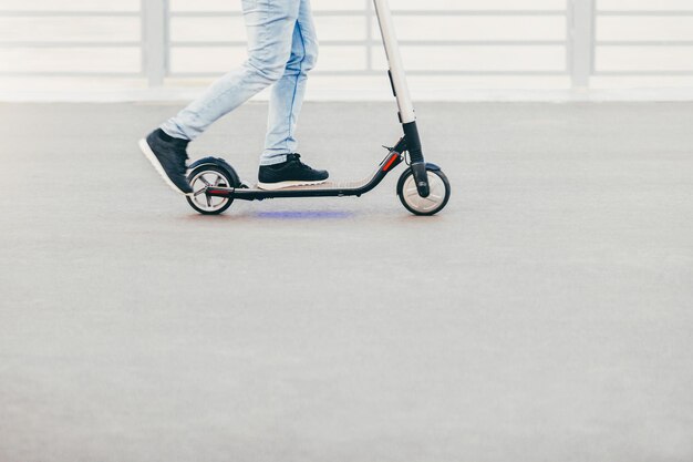 Scatto all'aperto di un uomo in scarpe da ginnastica e jeans che viene fotografato in movimento mentre guida uno scooter elettrico Persone e concetto di stile di vita attivo