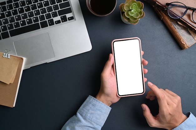 Scatto dall'alto dell'uomo d'affari seduto alla scrivania in ufficio e tenendo il telefono cellulare con lo schermo vuoto