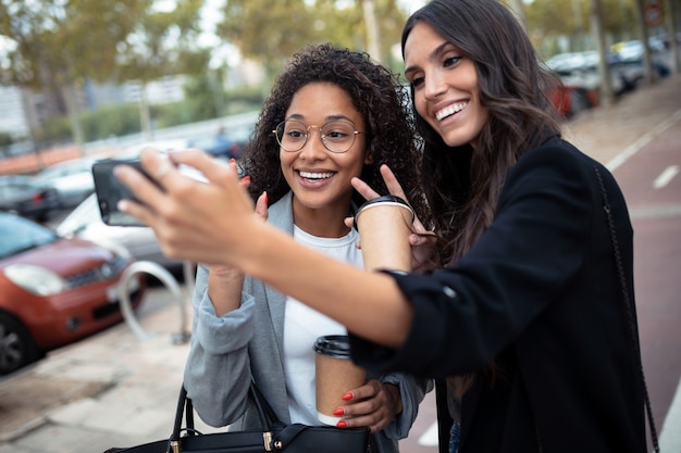 Scatto di due belle donne d'affari che fanno una videochiamata con uno smartphone mentre bevono caffè passeggiando per la città.