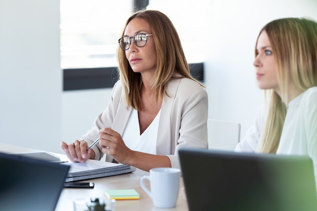 Scatto di due donne d'affari concentrate che ascoltano i suoi partner nello spazio di coworking.