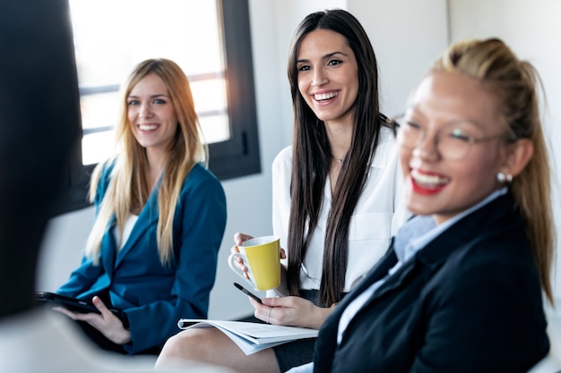 Scatto di tre eleganti giovani donne d'affari che guardano il suo collega mentre sorridono in ufficio.