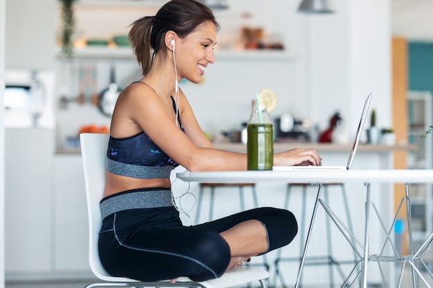 Scatto di una giovane donna sportiva che lavora con il suo laptop dopo una sessione di esercizi in cucina a casa.