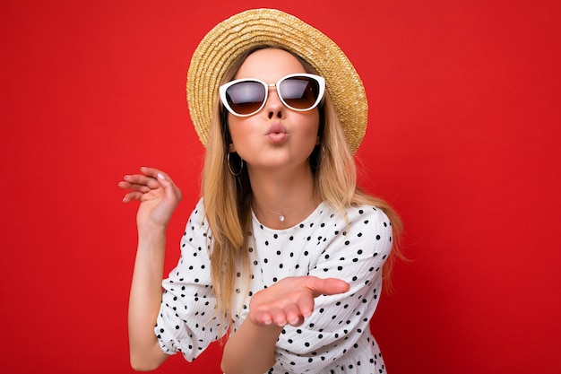 Scatto fotografico di una giovane bella donna bionda felice e carina che indossa occhiali da sole in abito casual e cappello di paglia