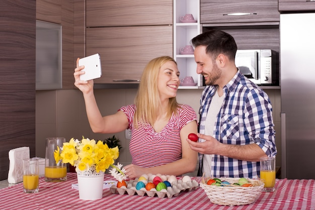 Scatto poco profondo di una coppia felice che si fa un selfie mentre dipinge le uova di Pasqua con gioia