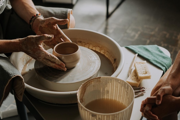 Scatto ravvicinato di una tazza di ceramica che gira sulla ruota del vasaio e le mani che modellano l'argilla