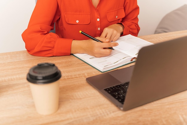 Scatto senza volto di una donna che lavora e scrive sul diario in ufficio