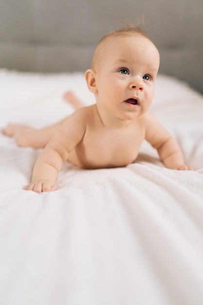 Scatto verticale di una piccola bambina carina sdraiata sullo stomaco sul letto che impara a tenere il ritratto della testa di