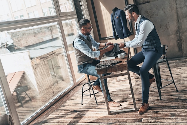 Scegliere il meglio. Giovane stilista alla moda che sceglie il tessuto con il suo cliente e sorride