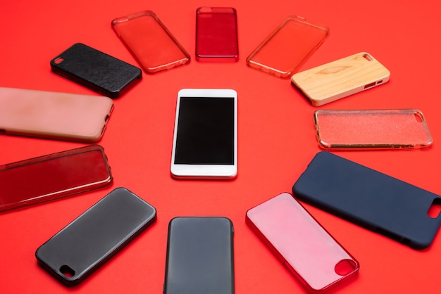 Scelta di cover posteriori in plastica multicolore per telefoni cellulari su sfondo rosso con uno smartphone sul lato