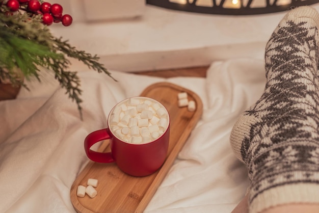 Scena accogliente di vibrazioni con una tazza di bevanda calda con marshmallow bianchi e piedi femminili in calda lana