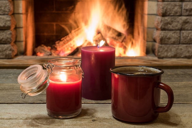 Scena accogliente vicino al camino con tazza di tè caldo, sciarpa calda e candele.