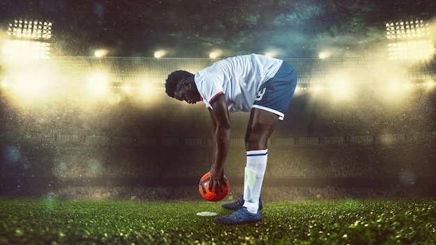 Scena di calcio durante la partita notturna con il giocatore in bianco e uniforme che posiziona la palla per calciare