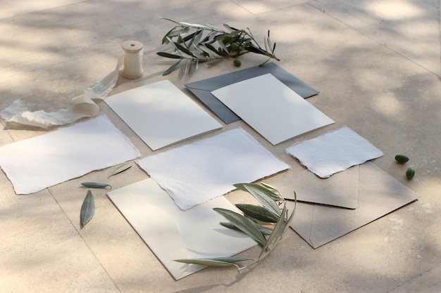 Scena di mockup di cancelleria per matrimoni estivi Buste di biglietti di auguri vuoti nastro di seta e rami di ulivo e frutta alla luce del sole Sfondo di marmo con ombre Vista dall'alto piatta femminile