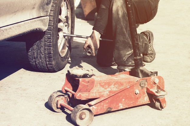 Scena di ruggine e fango del processo di perair delle ruote con lo stile di vita del martinetto idraulico rosso da pavimento.