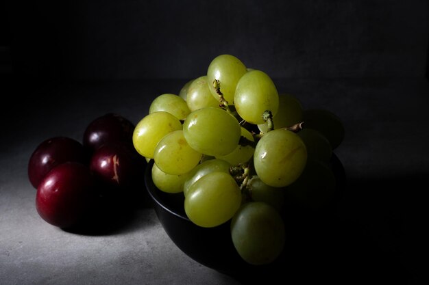 Scena in stile Darkfood con un grappolo d'uva verde e alcune prugne rosse fresche