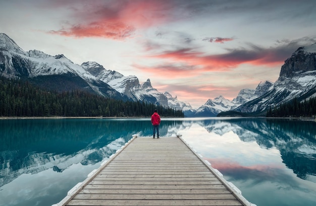 Scenario di Spirit Island con il viaggiatore maschio che si gode sul molo al tramonto nel parco nazionale di Jasper del lago Maligne in Canada