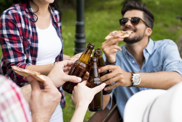 Scenario soleggiato di un gruppo di amici caucasici che brindano con le loro bottiglie di birra in un parco