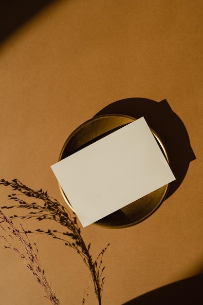 Scheda di carta bianca con spazio di copia di mockup su piastra d'oro Sfondio di zenzero con silhouette di ombre di luce solare Erba secca Vista superiore piatta