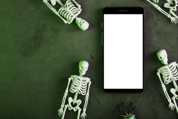 Scheletri decorativi si trovano vicino allo smartphone su uno sfondo scuro. Decorazione di Halloween, Vista dall'alto, Spazio libero