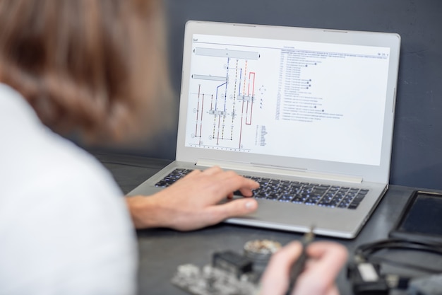 Schema del microcircuito. Vista posteriore dell'uomo che tiene il saldatore l'altra mano sulla tastiera del laptop, nessun volto visibile