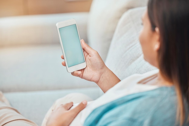 Schermata verde del telefono della donna incinta e mock up sul divano per la pubblicità o la promozione del marketing Chiave cromatica della gravidanza e femmina con smartphone mobile per inviare messaggi di testo ai social media o alla navigazione in Internet