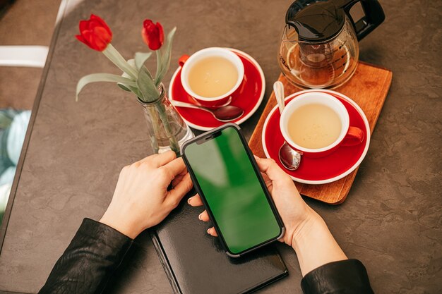 Schermo del telefono Chroma Key nelle mani di una donna che beve il tè in un bar con spazio per le copie