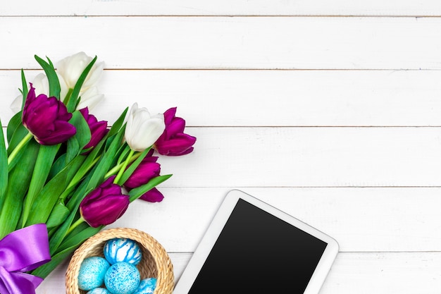 Schermo tablet per messaggio e tulipani colorati e uova di Pasqua su fondo in legno