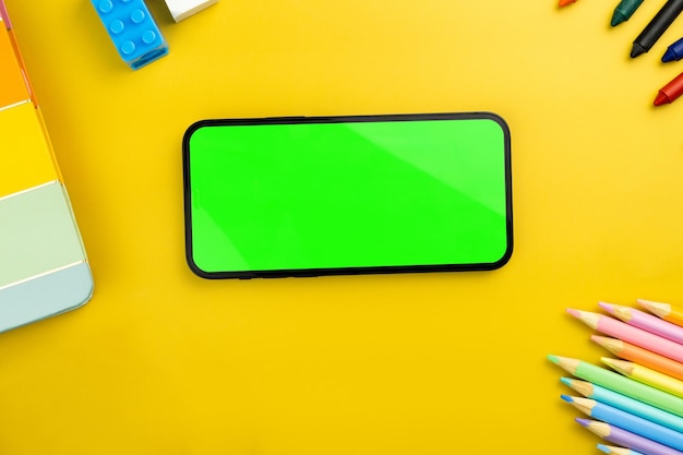 Schermo verde sullo smartphone Sfondo giallo con materiale scolastico accessori per bambini controller per videogiochi Chroma Key