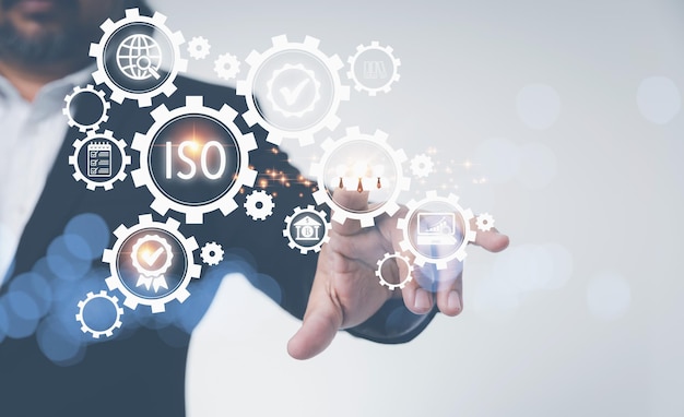 Schermo virtuale ISO con icone aziendali sugli ingranaggi ISO Standard certificazione standardizzazione concetto di controllo qualità Uomo d'affari che tocca l'icona del team di persone con certificazione e standardizzazione