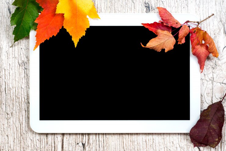 Schermo vuoto del nero della compressa di Digital con le foglie di autunno variopinte sulle plance di legno bianche