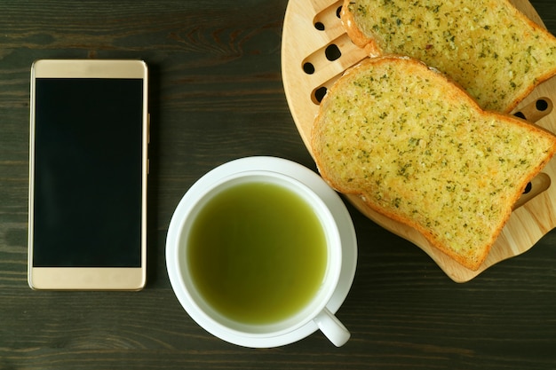 Schermo vuoto Smartphone con una tazza di tè verde e pane tostato burro aglio su oscurità