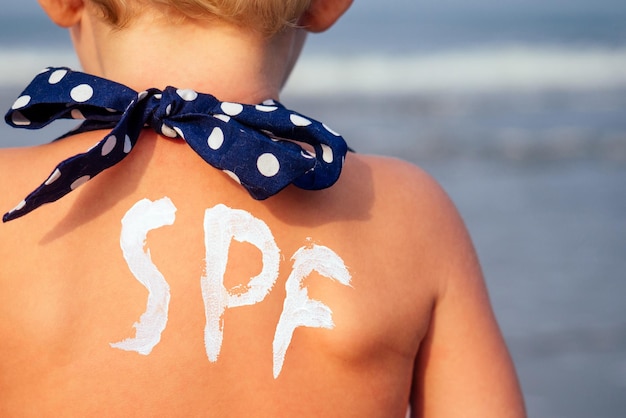 Schiena e spalle chiudono la figlia bionda di un anno dai capelli biondi usa una crema solare spf sulla spiaggia del mare dell'Oceano Indiano.