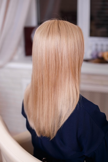 Schiena femminile con capelli biondi naturali lunghi lisci nel salone di parrucchiere