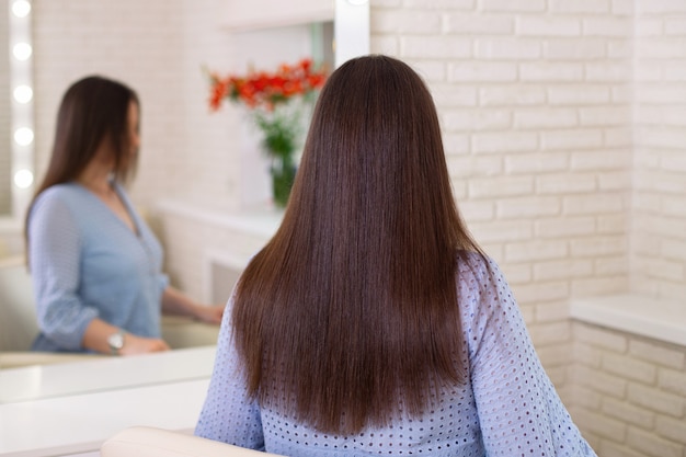 Schiena femminile con capelli castani lunghi e lisci nel salone di parrucchiere