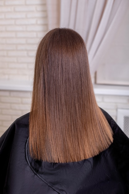 Schiena femminile con capelli castani lunghi e lisci nel salone di parrucchiere