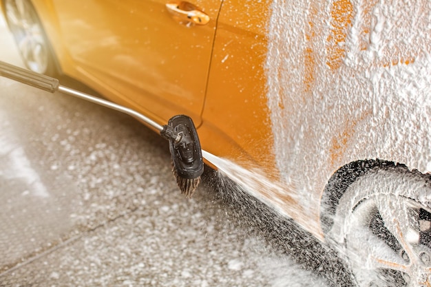 Schiuma e sapone spruzzati dalla spazzola sulla ruota posteriore dell'auto lavata nell'autolavaggio.