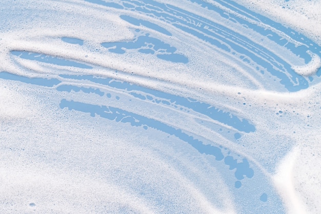 Schiuma saponosa bianca su sfondo blu. Concetto di pulizia/lavaggio.