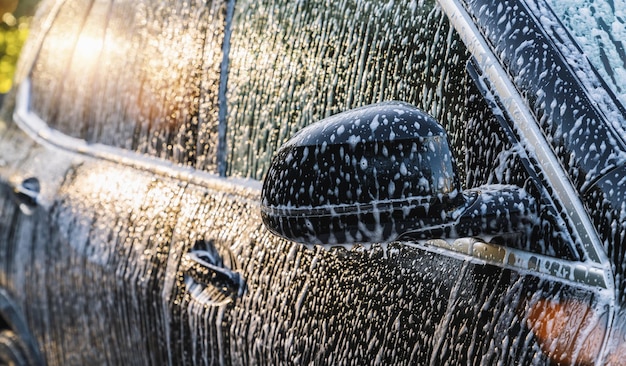 schiuma su un'auto nera, lavaggio di un'auto in un servizio di lavaggio, immagine di sfondo