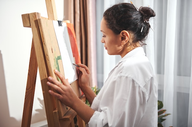 Schizzo del disegno della donna castana dell'artista o del progettista usando la matita e stando davanti al cavalletto