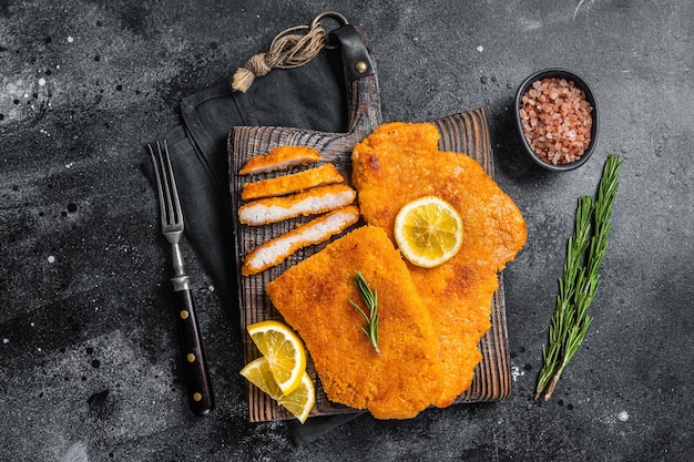 Schnitzel fritta affettata su una tavola di legno con erbe aromatiche Sfondo nero Vista dall'alto