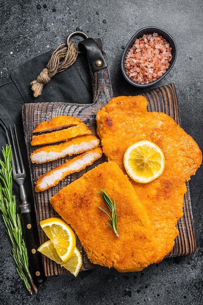 Schnitzel fritta affettata su una tavola di legno con erbe aromatiche Sfondo nero Vista dall'alto