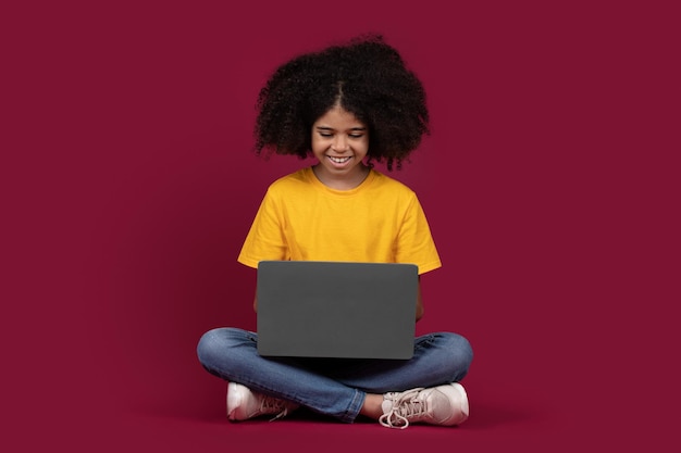Schooler nero allegro della ragazza che utilizza il fondo variopinto del computer portatile