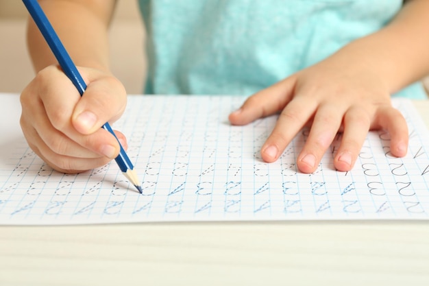 Schoolkid impara a scrivere sul primo piano del foglio di carta