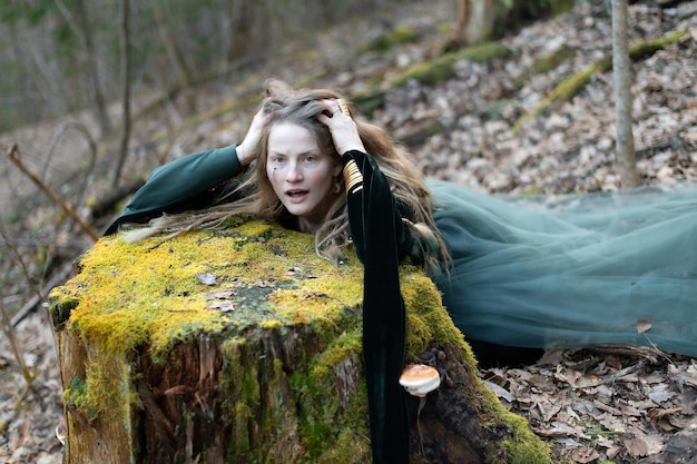 Sciamano femminile nella natura della foresta incontaminata sdraiata sul tronco verde dell'albero gioielli d'oro capelli pelosi